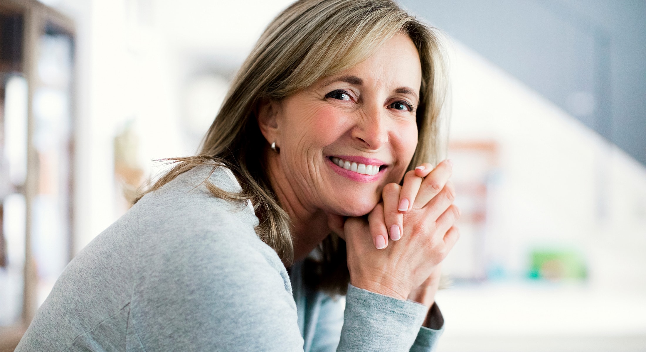 Smiling woman with hands clasped, indoors.