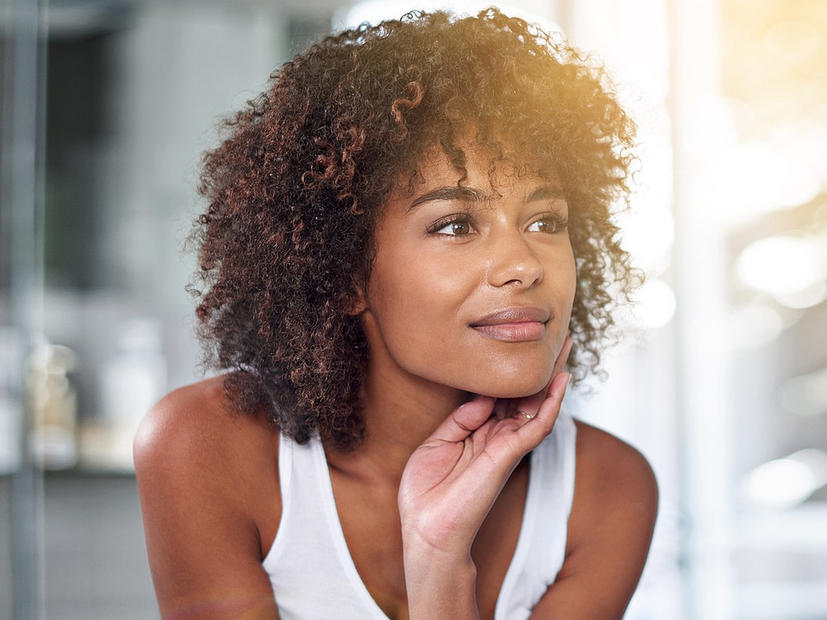 Thoughtful woman with curly hair in bright setting.